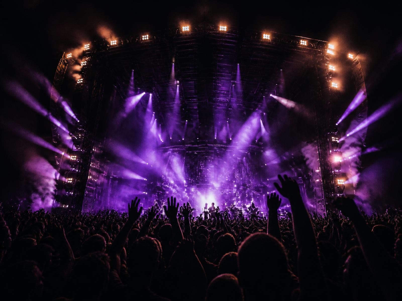 Crowd with raised hands in front of a stage flooded with violet light beams